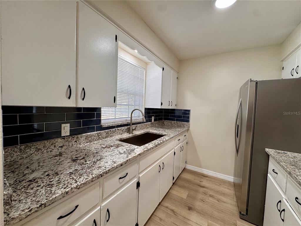 A kitchen features white cabinets, granite countertops, a dark tile backsplash, and stainless steel appliances — 791 LAKE AVENUE UNIT 2, CLERMONT, FL