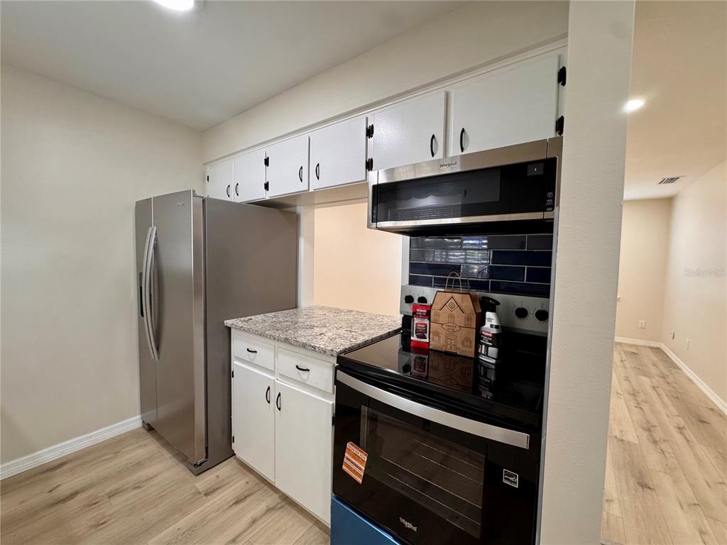 A kitchen features white cabinets, granite countertops, stainless steel appliances, and wood-look flooring — 791 LAKE AVENUE UNIT 2, CLERMONT, FL