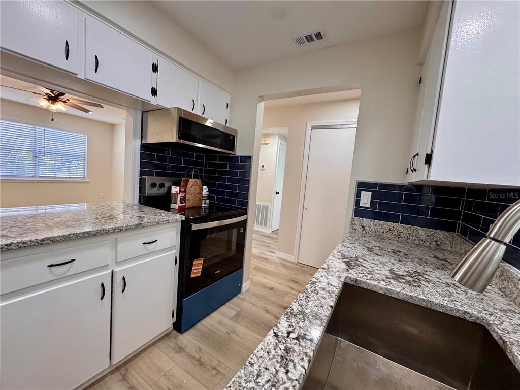 A kitchen features white cabinets, granite countertops, a dark blue tile backsplash, and stainless appliances — 791 LAKE AVENUE UNIT 2, CLERMONT, FL