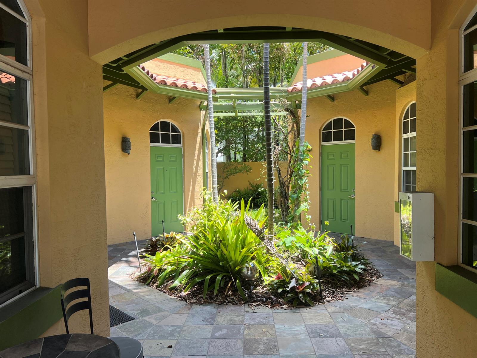 A central courtyard with a circular garden, stone tile flooring, and two green arched doors — 720 NE 3rd, Fort Lauderdale FL 33304, FORT LAUDERDALE, FL