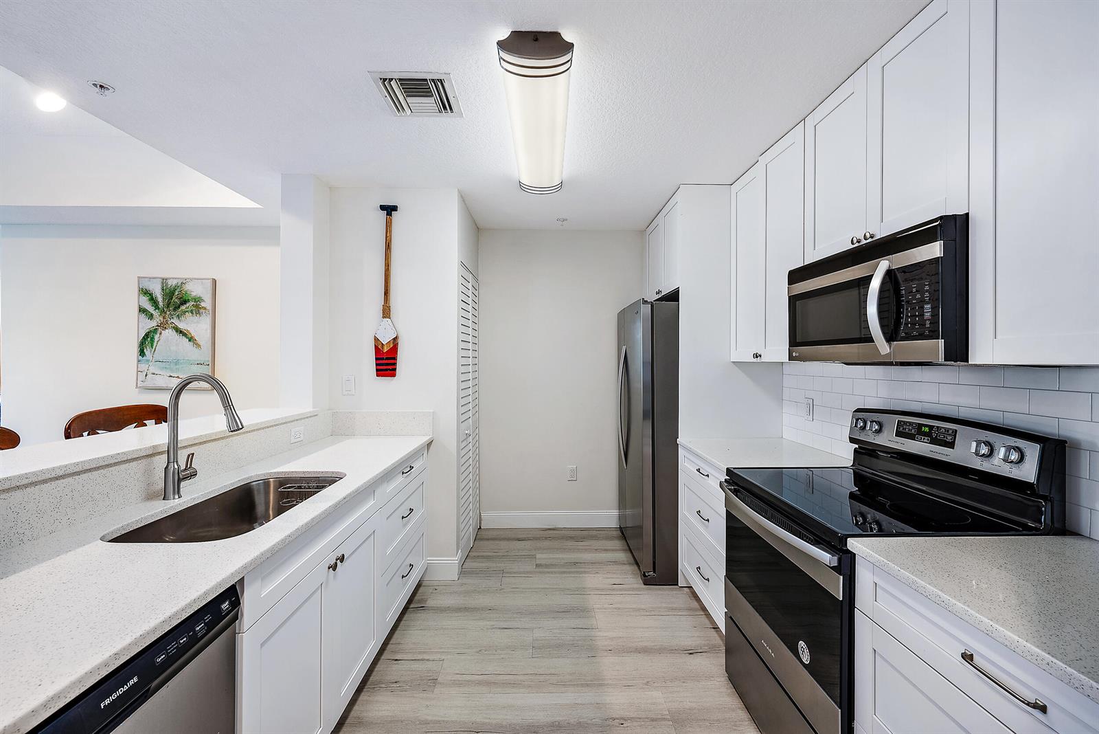 A kitchen with white cabinets, stainless steel appliances, quartz countertops, and light wood-look flooring — 1203 Town Center Drive # 201, Jupiter FL 33458, JUPITER, FL