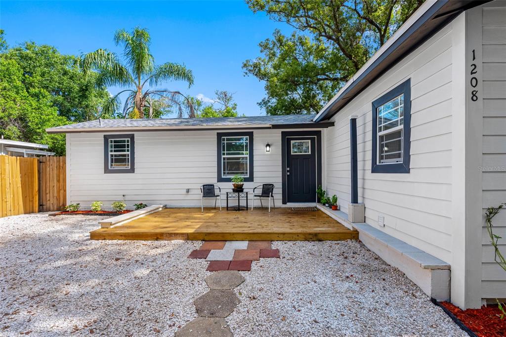 A white house exterior features a wooden deck, a dark front door, and gravel landscaping — 1208 E CHILKOOT AVENUE, TAMPA, FL