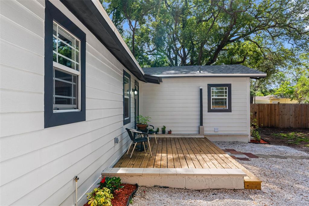 A white house exterior features a wooden deck, dark window trim, and a gravel yard — 1208 E CHILKOOT AVENUE, TAMPA, FL