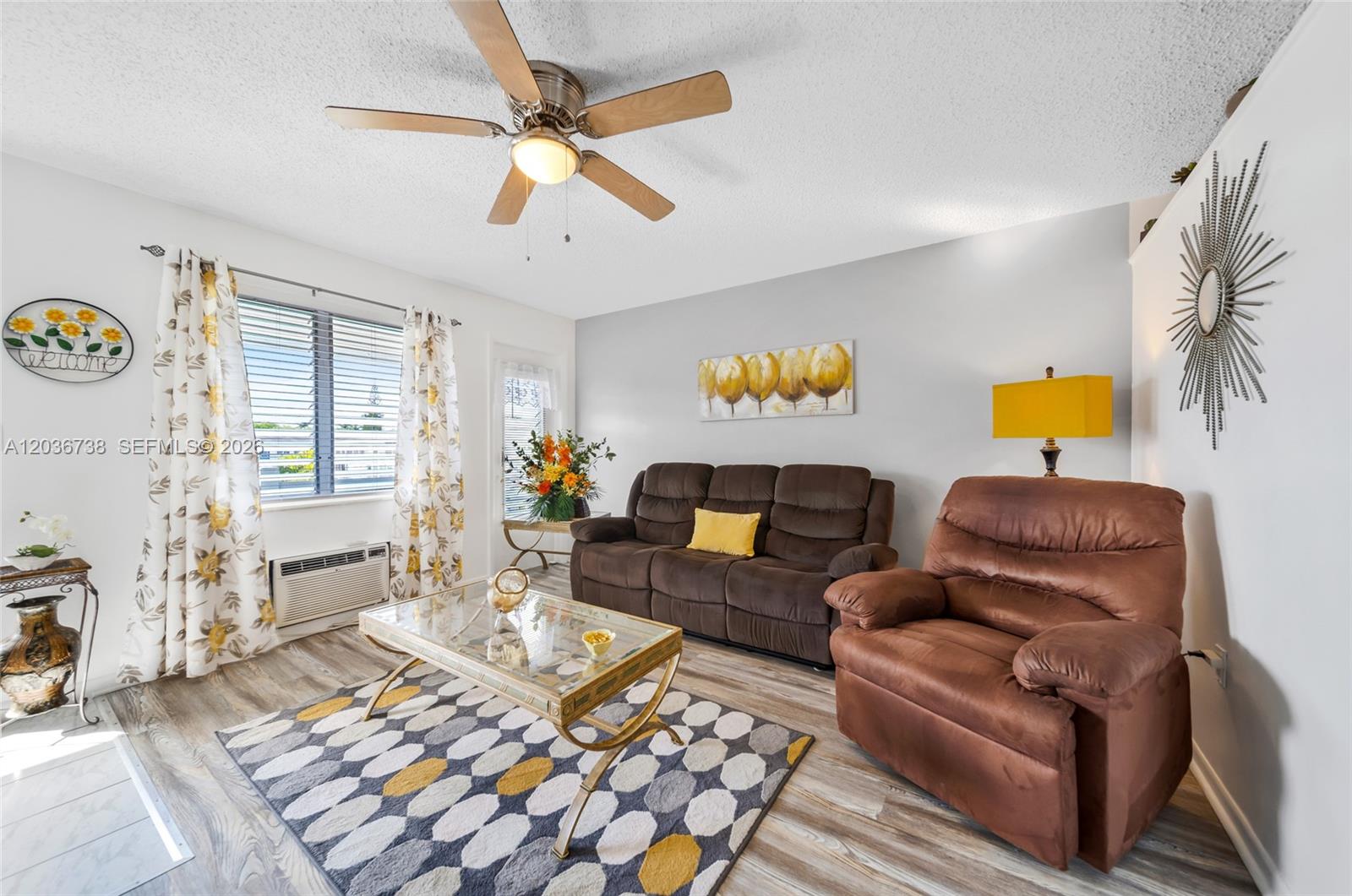 A living room features a brown sofa and recliner, a glass coffee table, and patterned curtains — 15610 NE 6th Ave # 34C, Miami FL 33162, MIAMI, FL