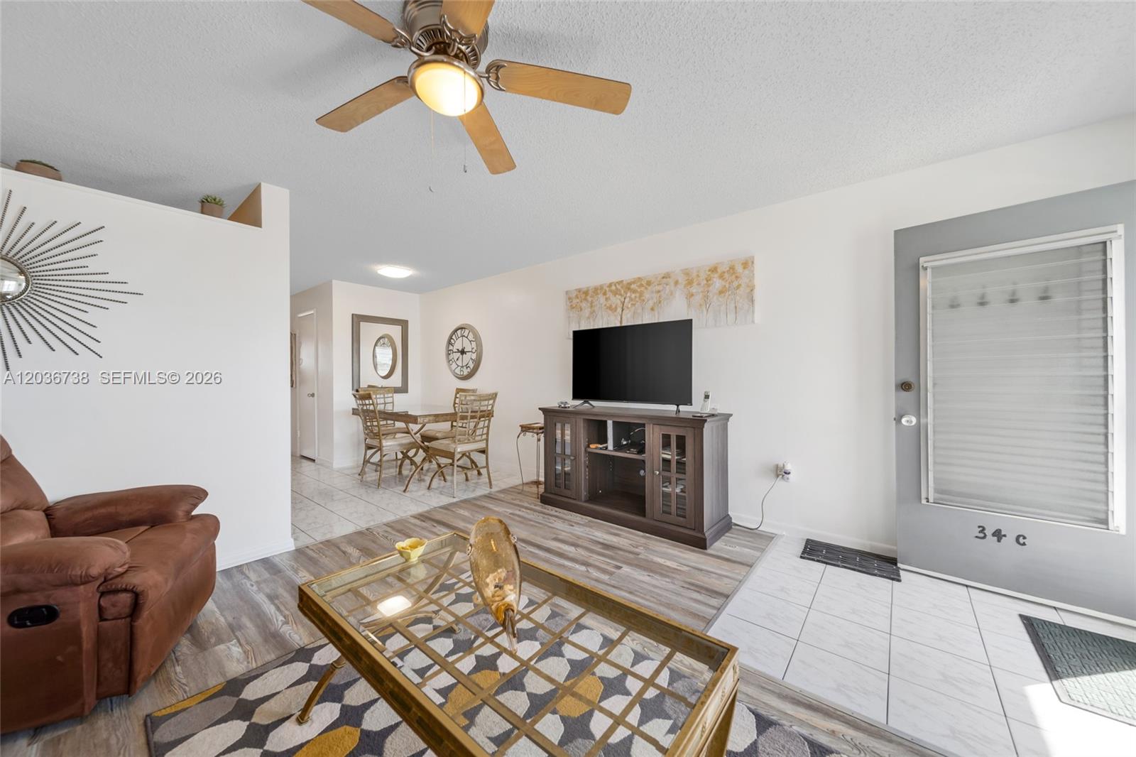 A living room features a ceiling fan, wood-look flooring, a television console, and dining area — 15610 NE 6th Ave # 34C, Miami FL 33162, MIAMI, FL