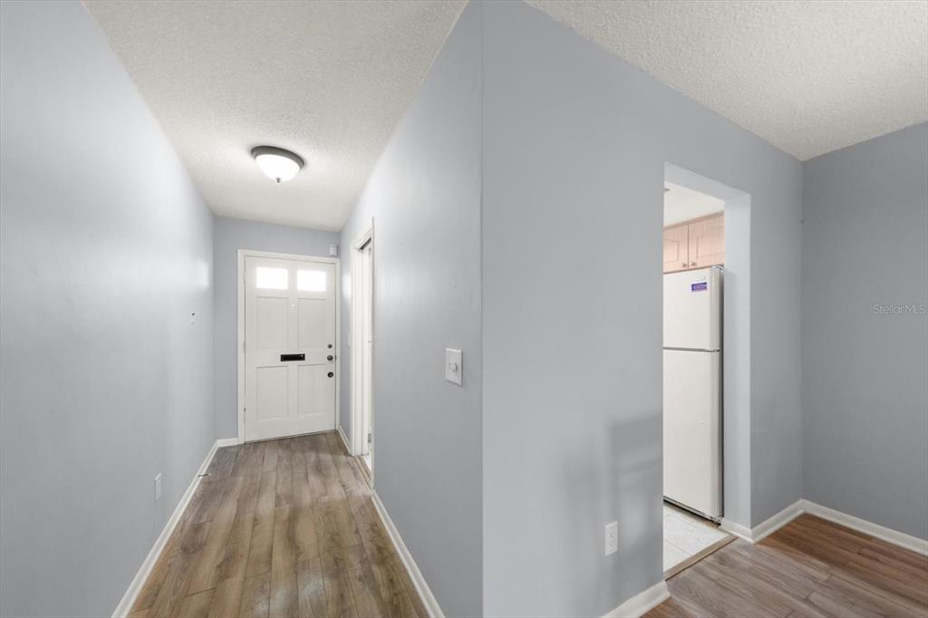 A hallway with wood-look flooring leads to a white front door and a kitchen area — 1668 S LAKE AVENUE UNIT 2, CLEARWATER, FL