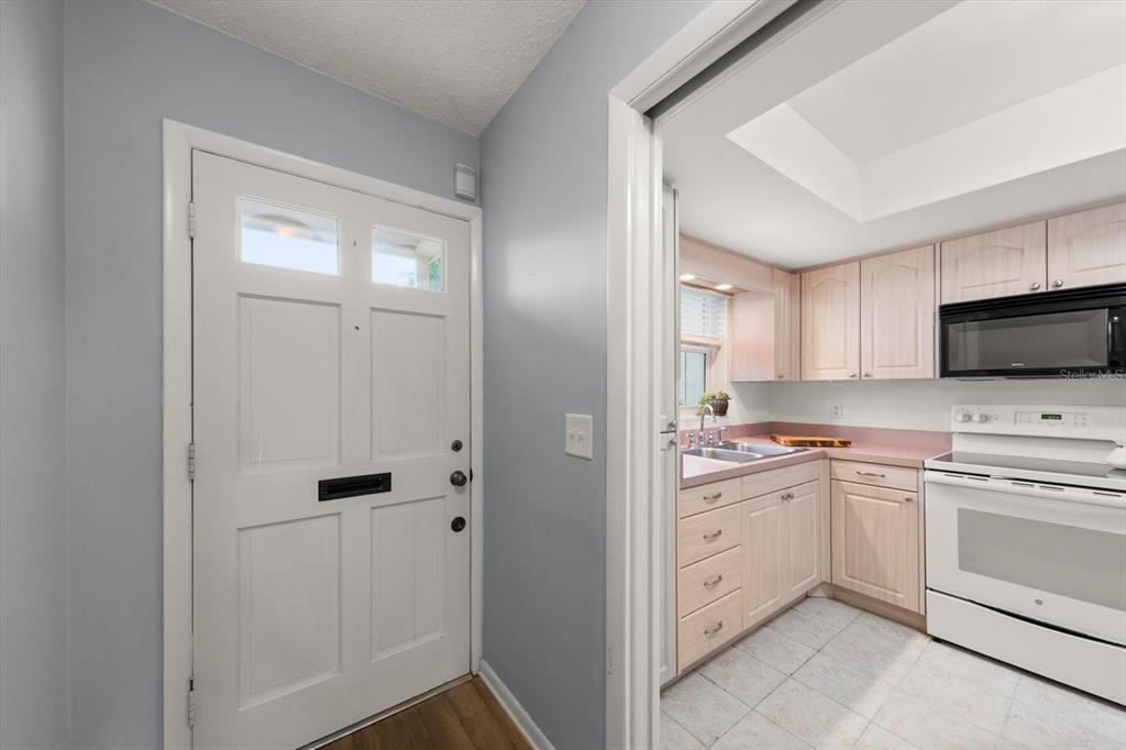 A white front door stands next to a kitchen with light wood cabinets and countertops — 1668 S LAKE AVENUE UNIT 2, CLEARWATER, FL