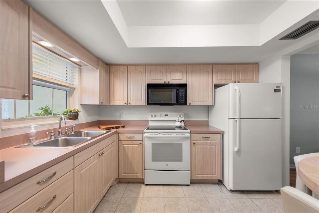A kitchen features light wood cabinets, a white stove, a microwave, and a white refrigerator — 1668 S LAKE AVENUE UNIT 2, CLEARWATER, FL