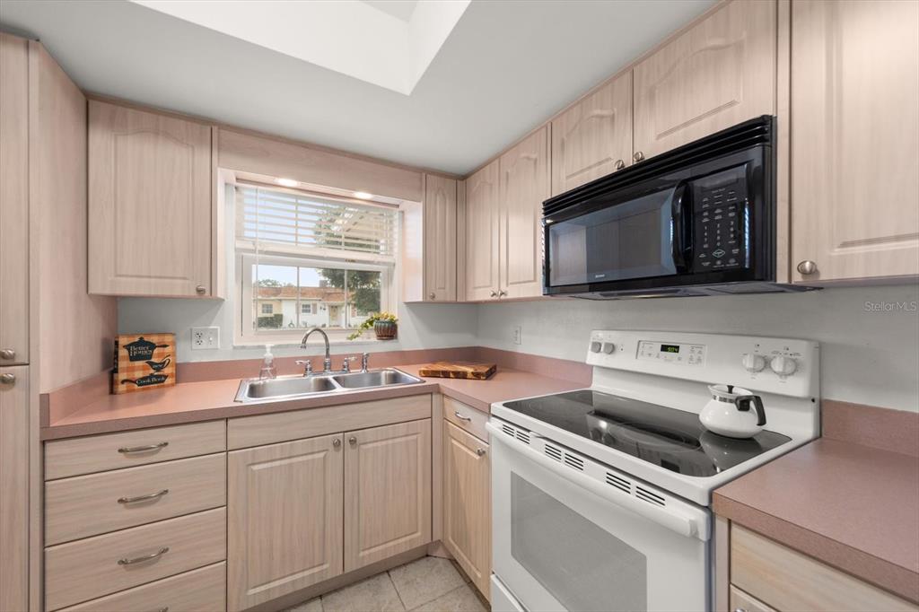 A kitchen features light wood cabinets, pink countertops, a double sink, and white appliances — 1668 S LAKE AVENUE UNIT 2, CLEARWATER, FL