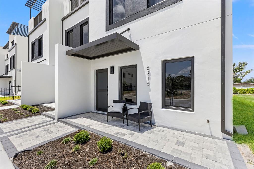 A modern white townhouse exterior features a paved entryway, a dark awning, and two chairs — 6218 64TH WAY N, PINELLAS PARK, FL