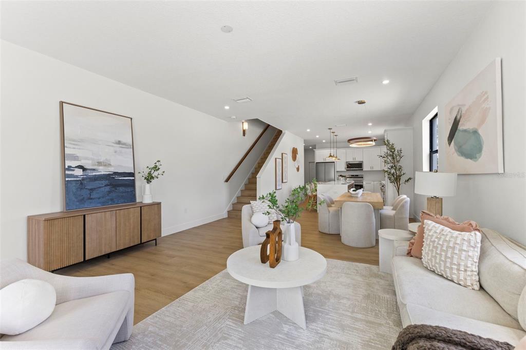 An open-concept living and dining area features light wood floors, white walls, and modern furniture — 6218 64TH WAY N, PINELLAS PARK, FL