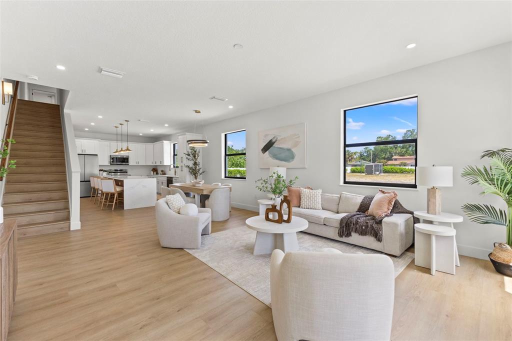 An open-concept living room and kitchen feature light wood flooring, white cabinetry, and a staircase — 6218 64TH WAY N, PINELLAS PARK, FL