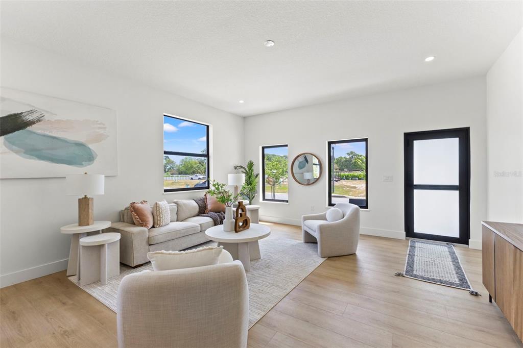 A bright living room features light wood flooring, neutral furniture, and a black-framed glass door — 6218 64TH WAY N, PINELLAS PARK, FL