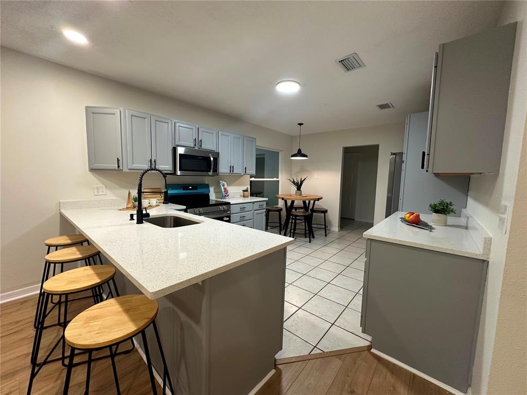 A kitchen features a quartz-topped island with bar stools, gray cabinetry, and tile flooring — 22360 STILLWOOD DRIVE, LAND O LAKES, FL
