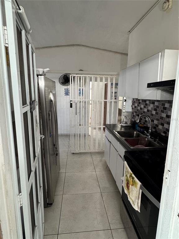 A narrow kitchen features white cabinets, a stainless steel refrigerator, and a metal security gate — N618 CALLE JULIO ANDINO, SAN JUAN, PR