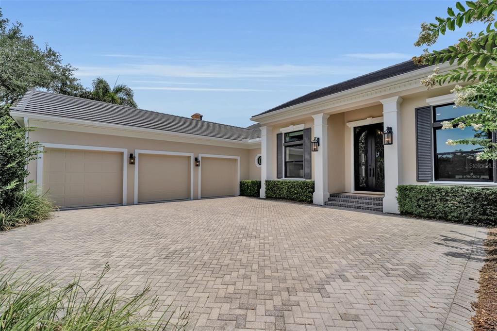 A beige house with a three-car garage and a paved driveway under a blue sky — 8986 BLOOMFIELD BOULEVARD, SARASOTA, FL
