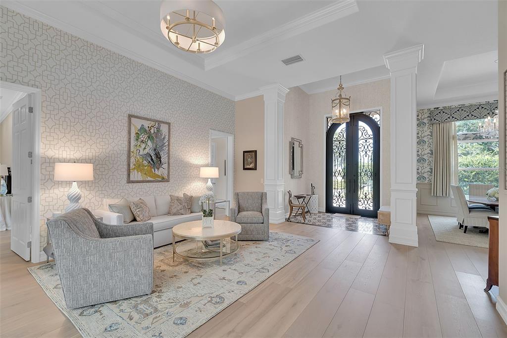 A bright living room features patterned wallpaper, light wood floors, and a double-door entryway — 8986 BLOOMFIELD BOULEVARD, SARASOTA, FL