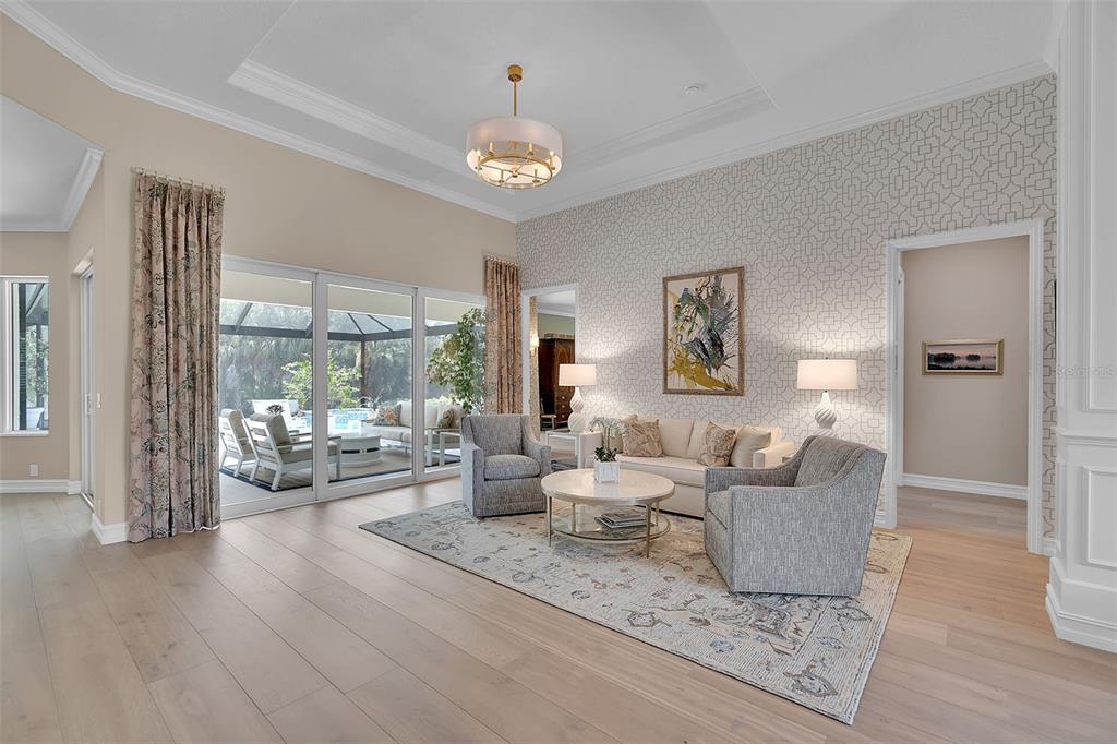 A living room features light wood floors, patterned wallpaper, a tray ceiling, and sliding glass doors — 8986 BLOOMFIELD BOULEVARD, SARASOTA, FL