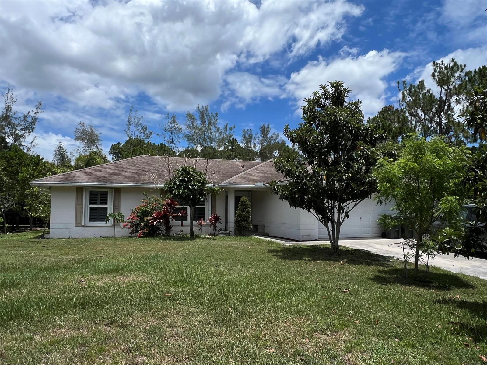 A single-story white house with a brown roof, a garage, and trees in the yard — 12403 N 87th St Street N, FL 33412, FL