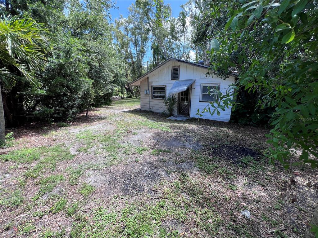 A small, white, single-story house sits on a dirt lot surrounded by trees — 0 TRINIDAD STREET, SARASOTA, FL