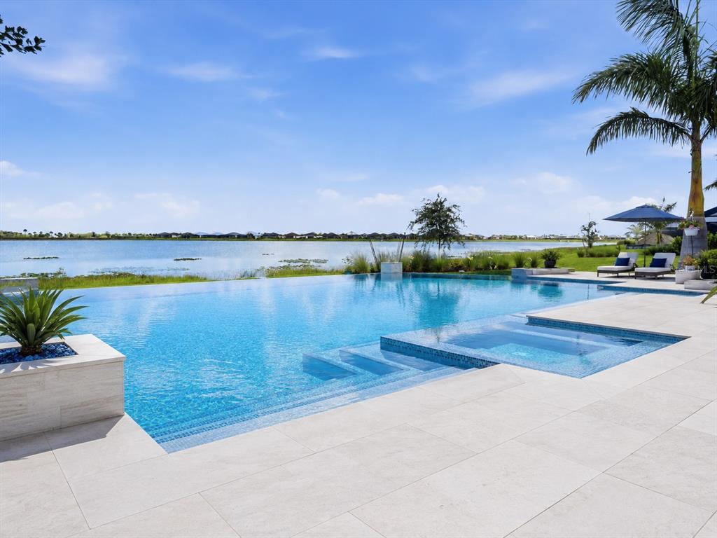 An infinity pool overlooks a lake with a spa and stone patio in the foreground — 16148 PRESERVATION BOULEVARD, PUNTA GORDA, FL