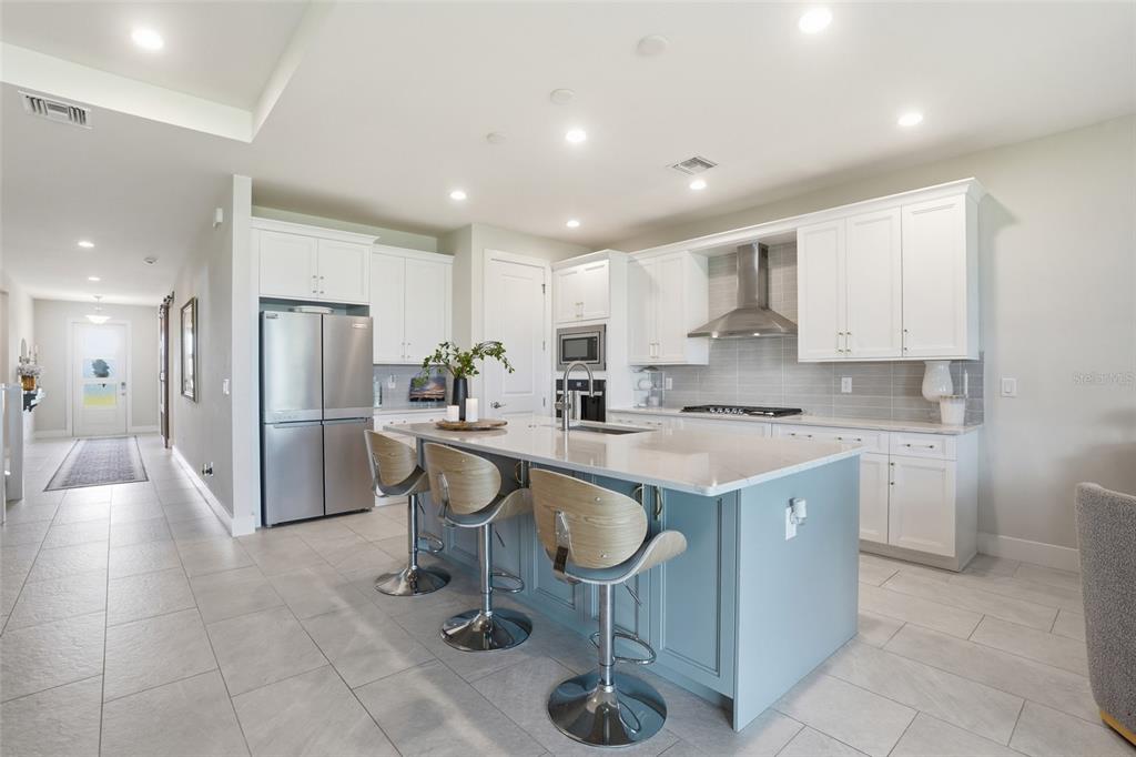 A modern kitchen features a light blue island with bar stools, white cabinetry, and stainless appliances — 16148 PRESERVATION BOULEVARD, PUNTA GORDA, FL