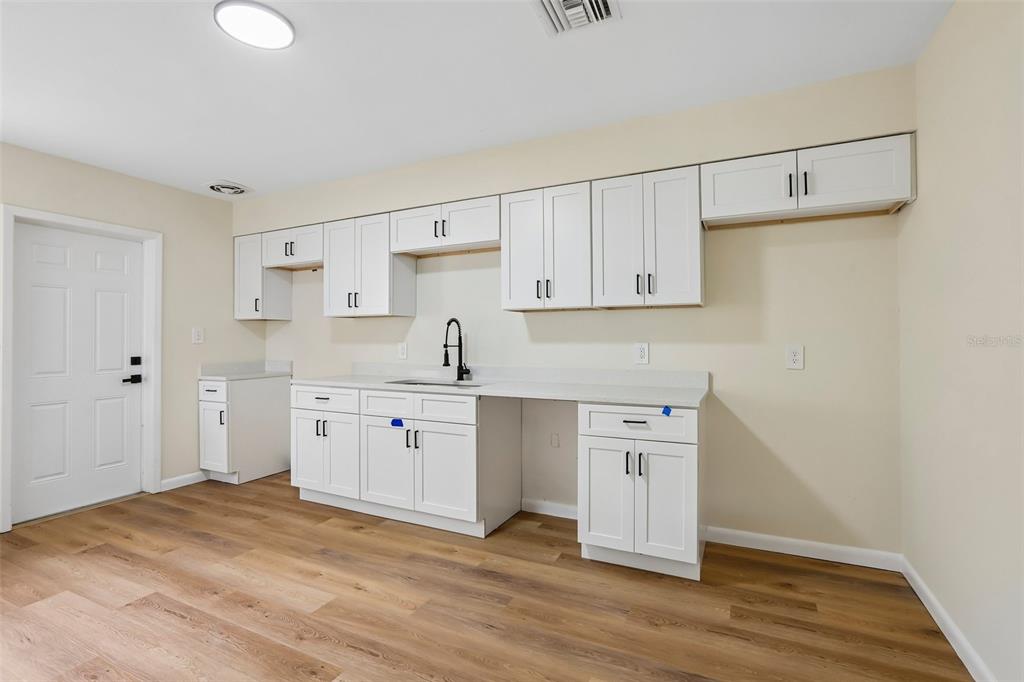 A kitchen features white cabinets, light countertops, a black faucet, and wood-look flooring — 2002 E IDLEWILD AVENUE, TAMPA, FL