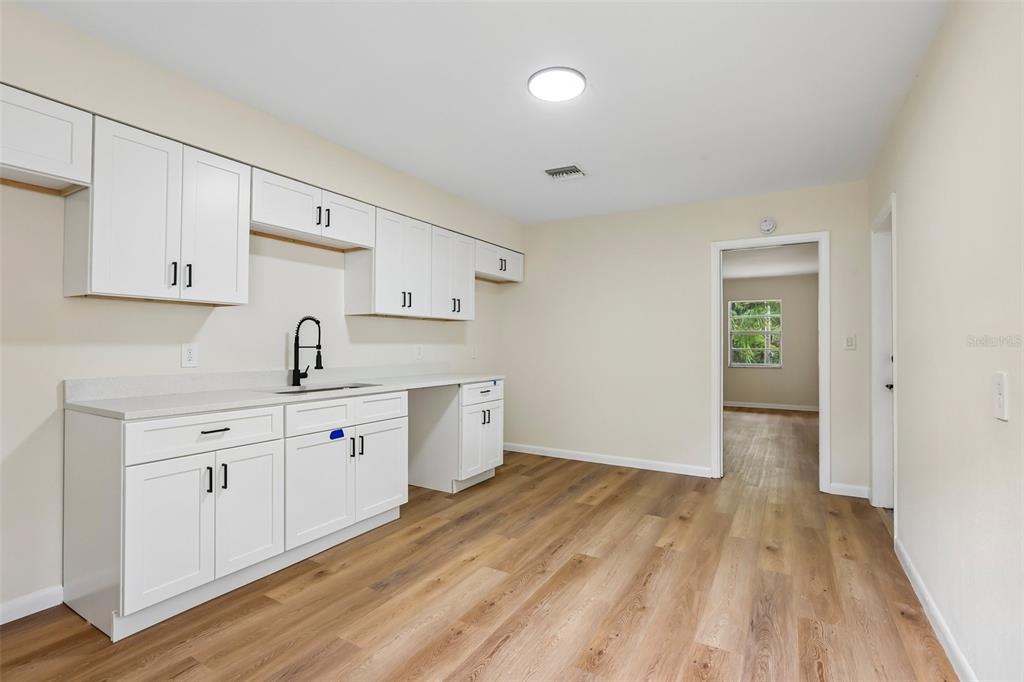A kitchen features white cabinets, a sink with a black faucet, and wood-look flooring — 2002 E IDLEWILD AVENUE, TAMPA, FL