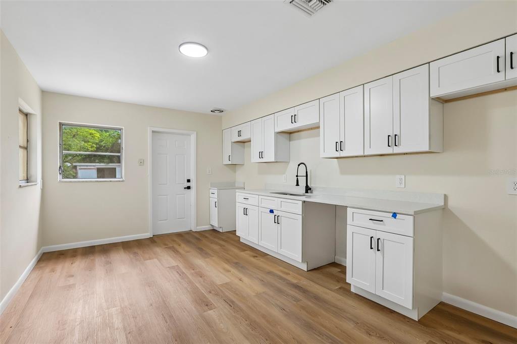A kitchen features white shaker cabinets, light countertops, a black faucet, and wood-look flooring — 2002 E IDLEWILD AVENUE, TAMPA, FL