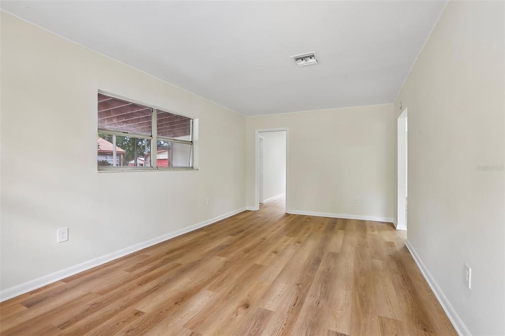 An empty room features light wood-look flooring, cream-colored walls, and a single window — 2002 E IDLEWILD AVENUE, TAMPA, FL