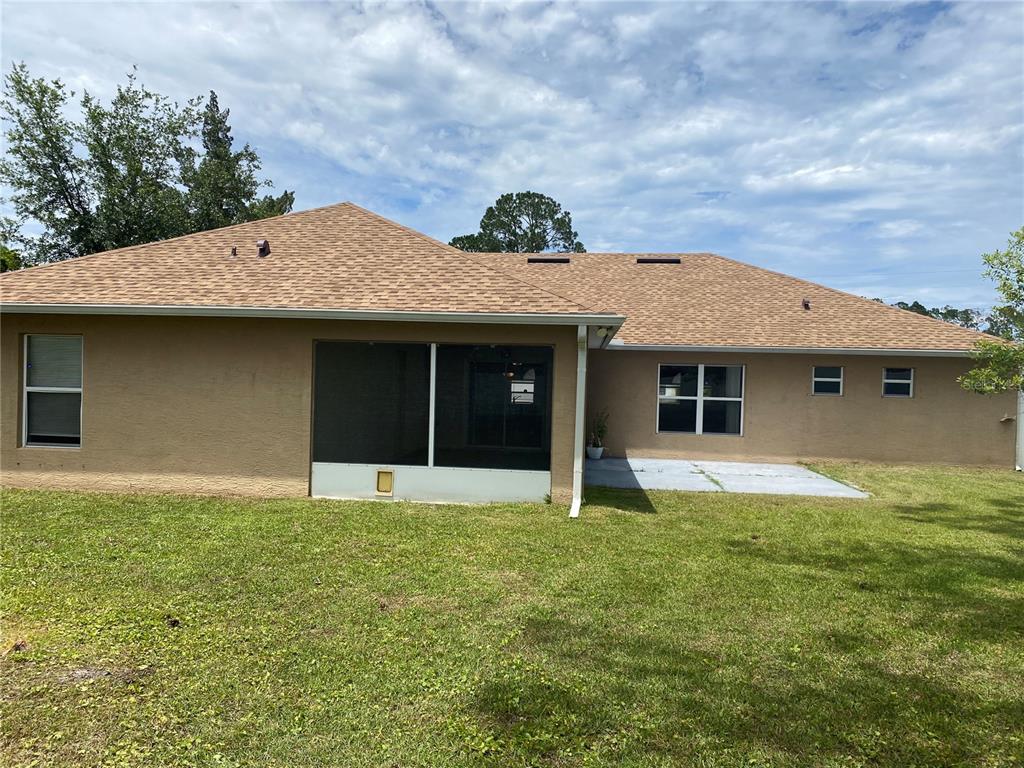 The rear exterior of a tan house features a screened-in porch and a concrete patio — 8 RENWORTH PLACE, PALM COAST, FL