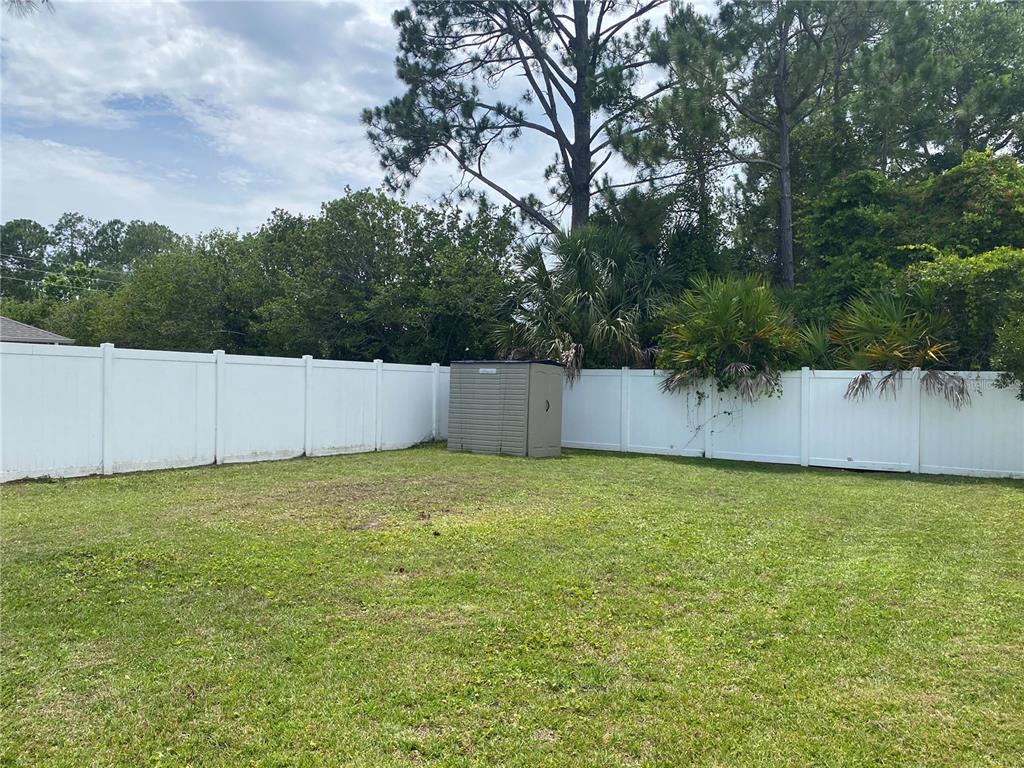 A grassy backyard features a white vinyl fence and a small storage shed — 8 RENWORTH PLACE, PALM COAST, FL