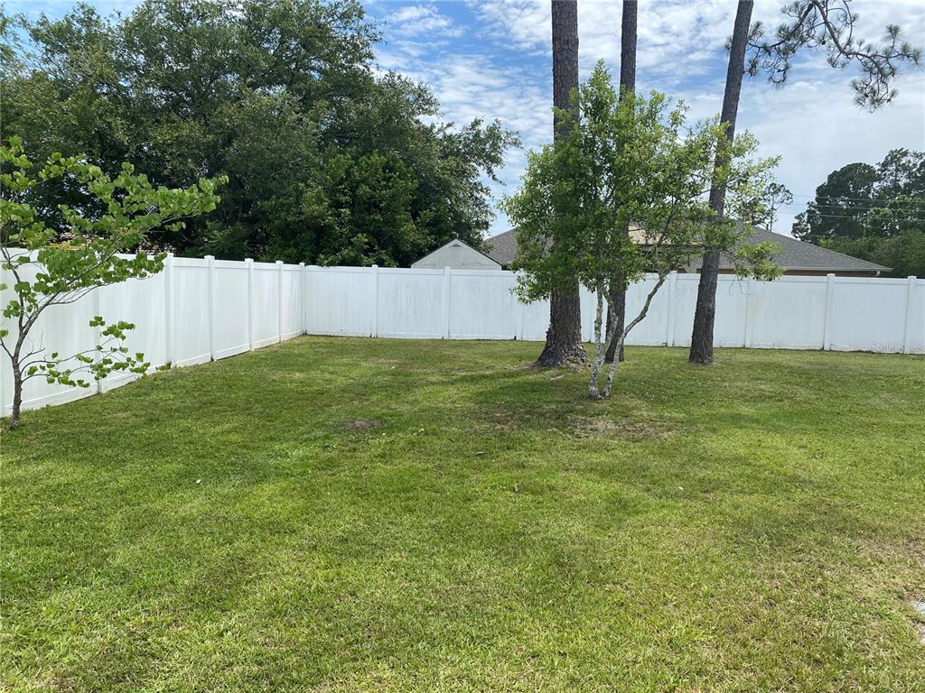 A grassy backyard features a white vinyl privacy fence and several mature trees — 8 RENWORTH PLACE, PALM COAST, FL