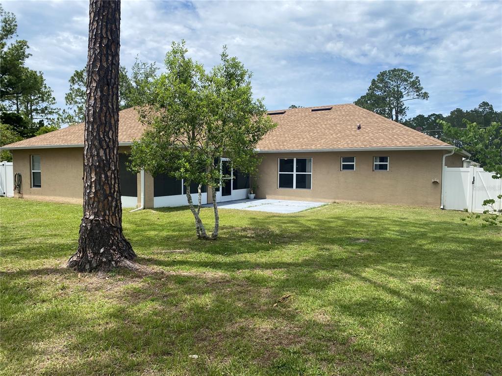 The rear exterior of a single-story house features a screened-in porch and a concrete patio — 8 RENWORTH PLACE, PALM COAST, FL