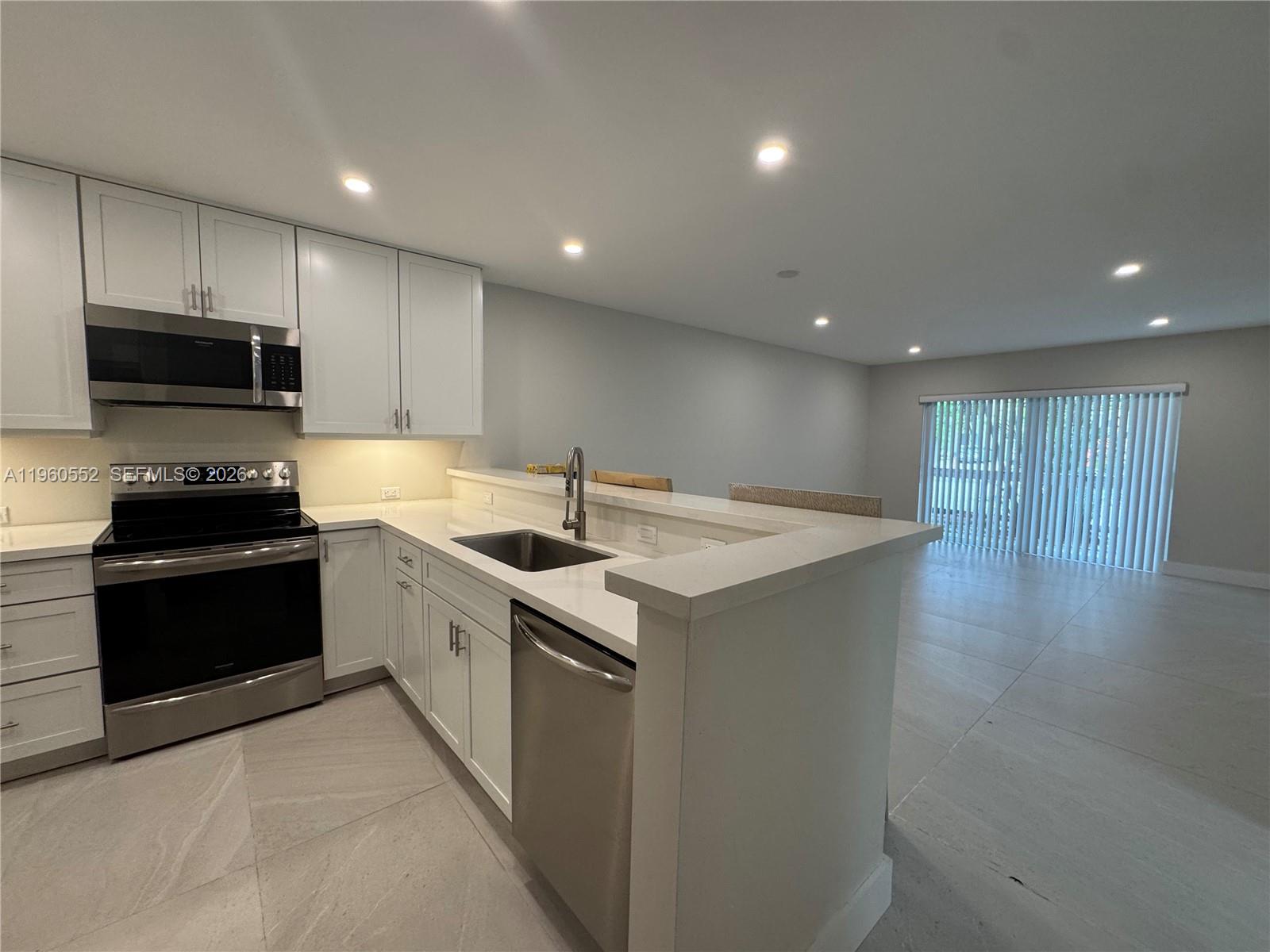 A modern kitchen features white cabinets, stainless steel appliances, and a quartz breakfast bar — 7810 Camino Real # 104, Miami FL 33143, MIAMI, FL