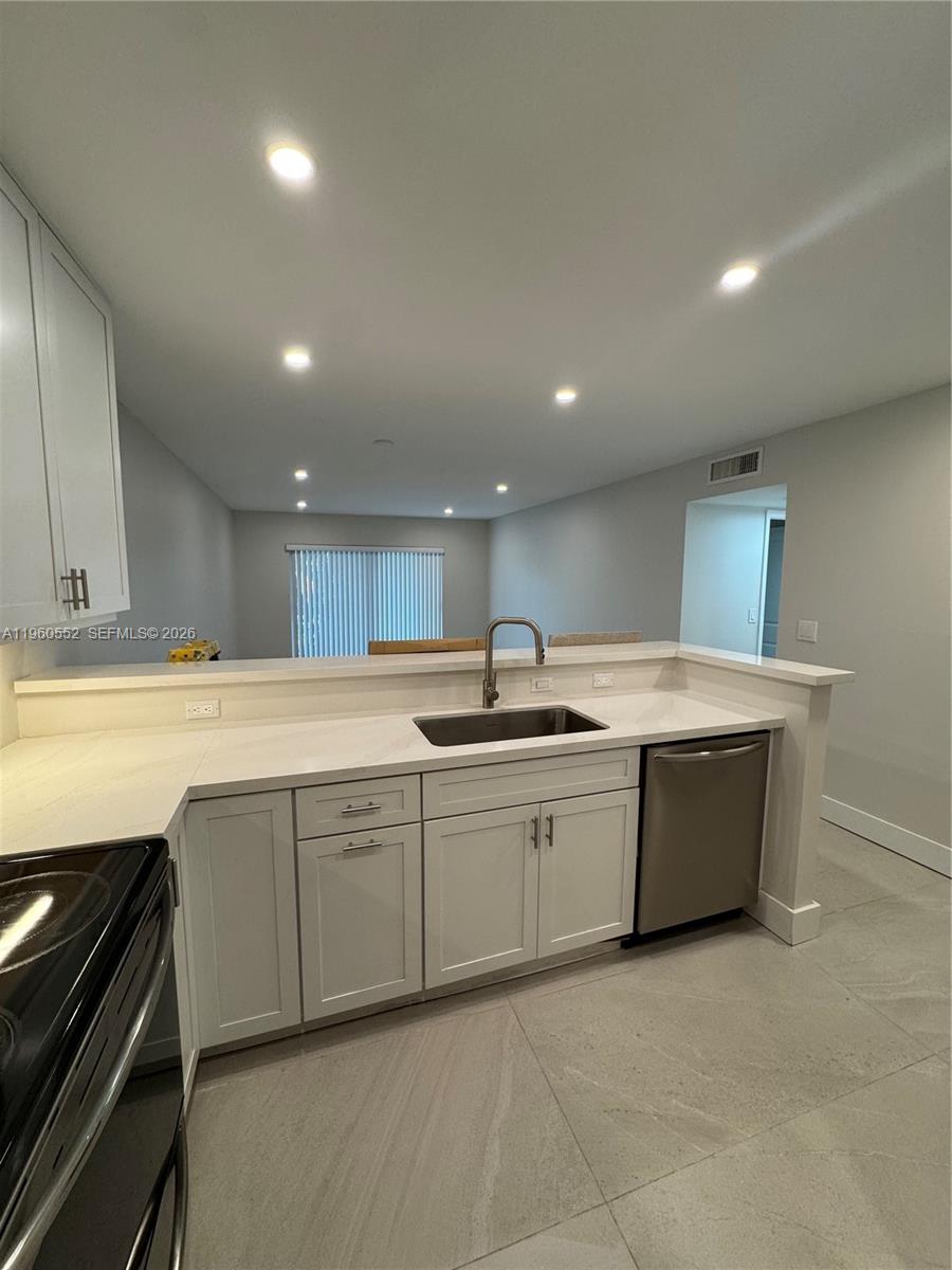 A kitchen features white cabinets, light countertops, stainless steel appliances, and large floor tiles — 7810 Camino Real # 104, Miami FL 33143, MIAMI, FL