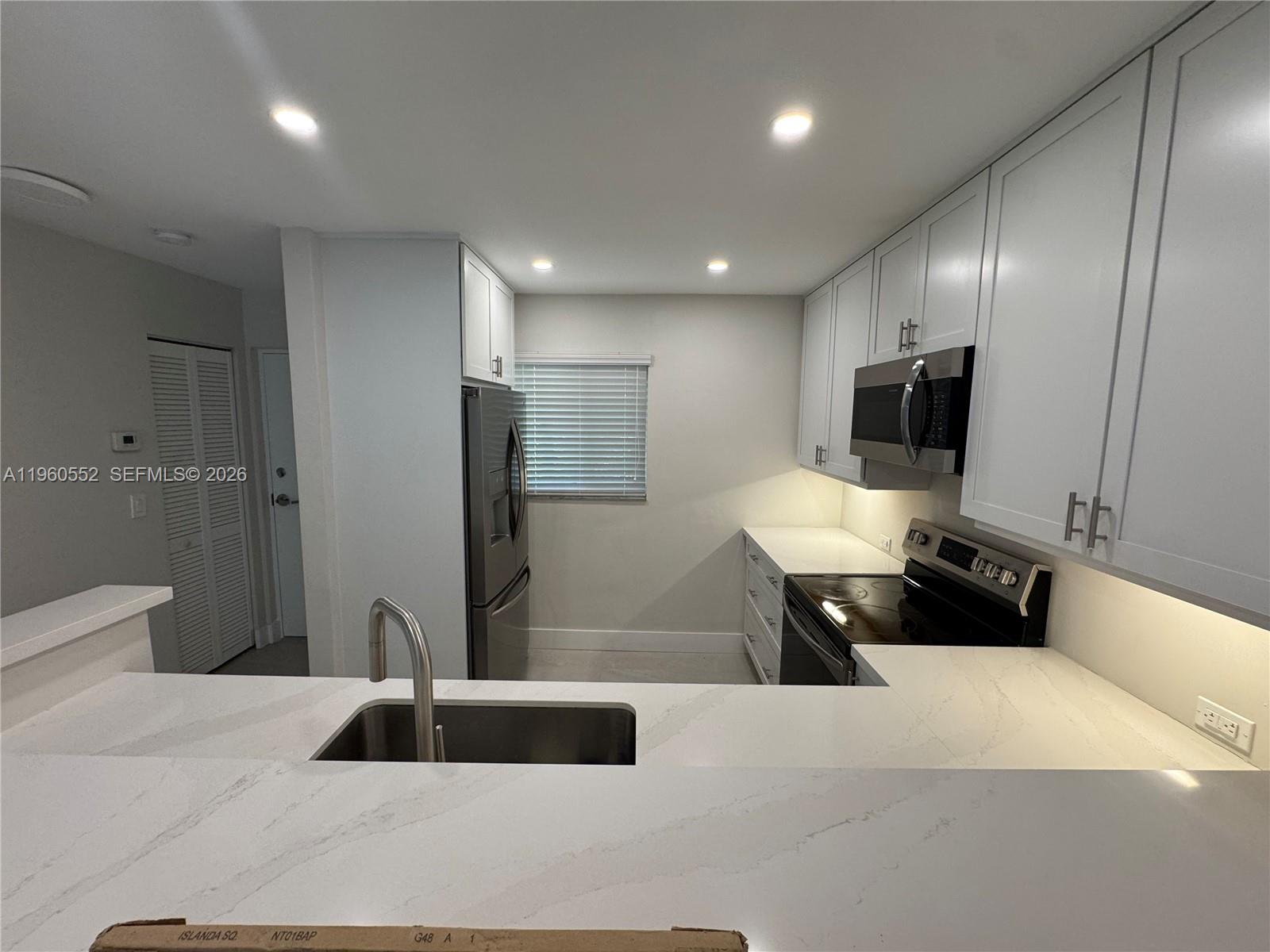 A modern kitchen features white cabinets, stainless steel appliances, and a white quartz countertop — 7810 Camino Real # 104, Miami FL 33143, MIAMI, FL