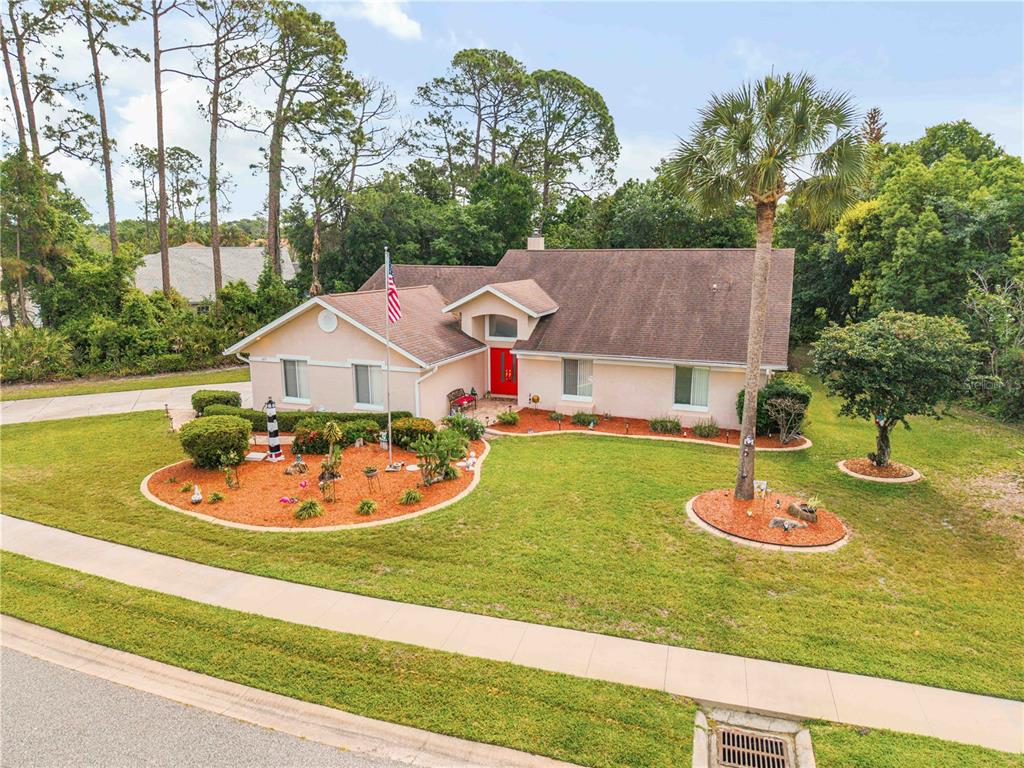 A single-story house with a red front door, a flagpole, and landscaped front yard beds — 107 MUIRFIELD DRIVE, DAYTONA BEACH, FL