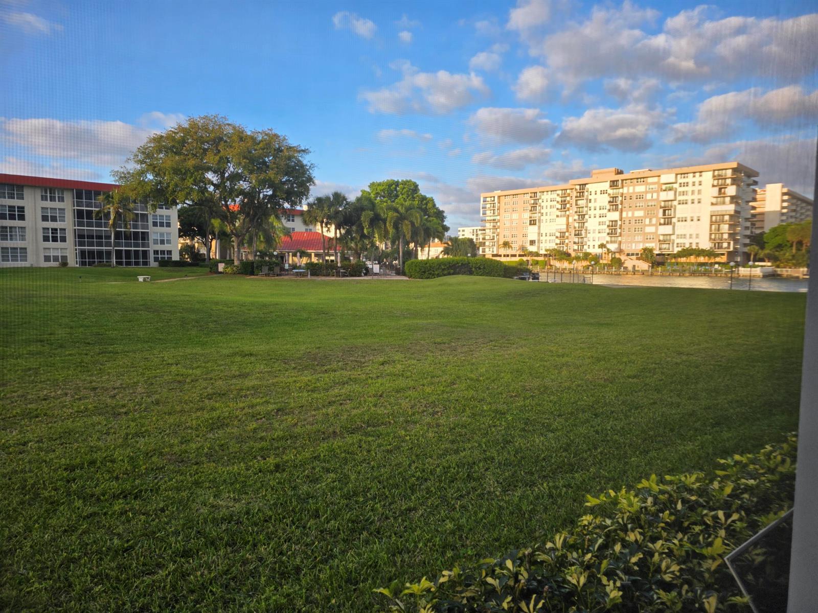A large grassy lawn sits between two apartment buildings under a blue sky — 3100 NE 48th Court # 113, Lighthouse Point FL 33064, LIGHTHOUSE POINT, FL