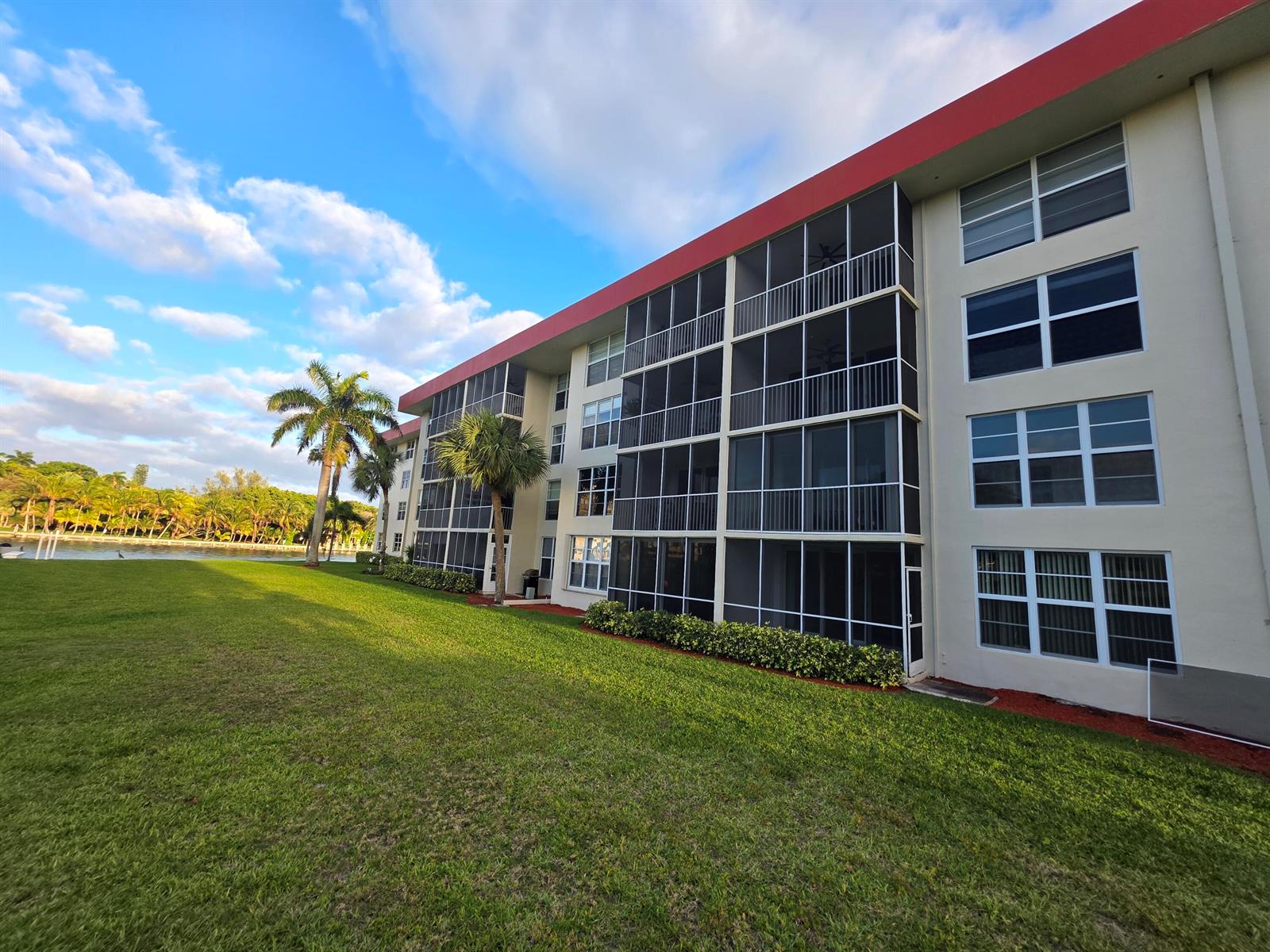 A multi-story apartment building with screened balconies sits next to a grassy lawn and water — 3100 NE 48th Court # 113, Lighthouse Point FL 33064, LIGHTHOUSE POINT, FL