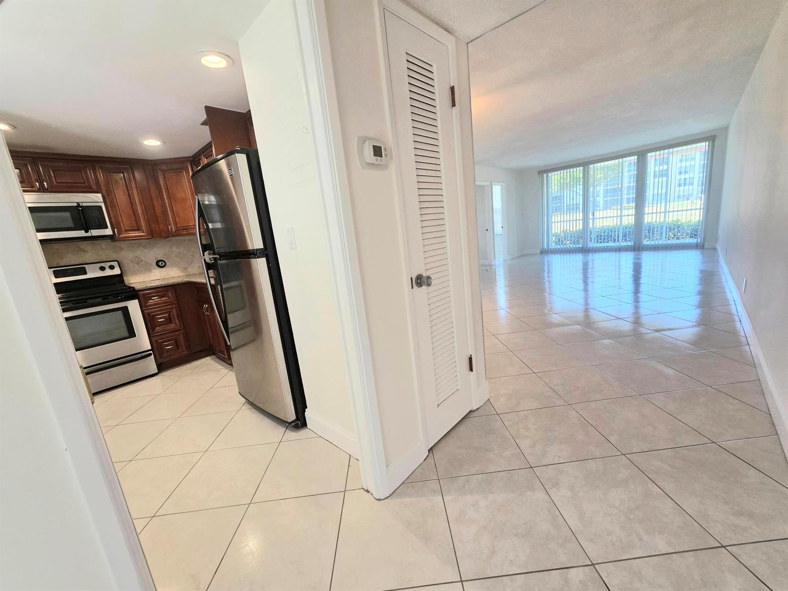 A kitchen with wood cabinets and stainless appliances opens to a tiled living area — 3100 NE 48th Court # 113, Lighthouse Point FL 33064, LIGHTHOUSE POINT, FL