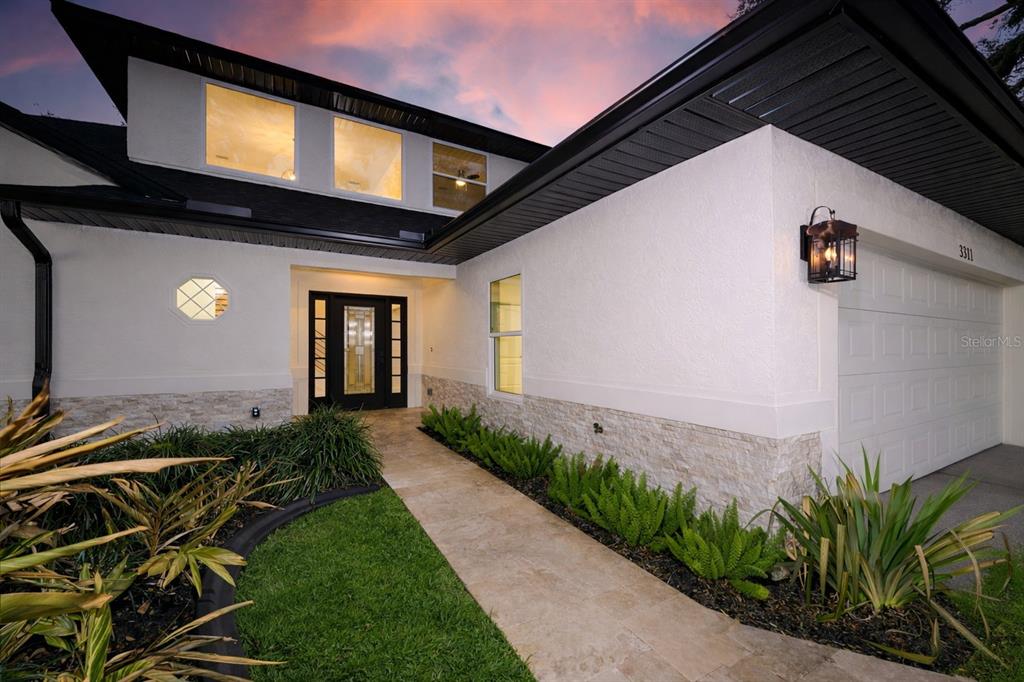 A modern house exterior features a white stucco facade, stone base, and a paved walkway — 3311 OAK VISTA DRIVE, PORT ORANGE, FL
