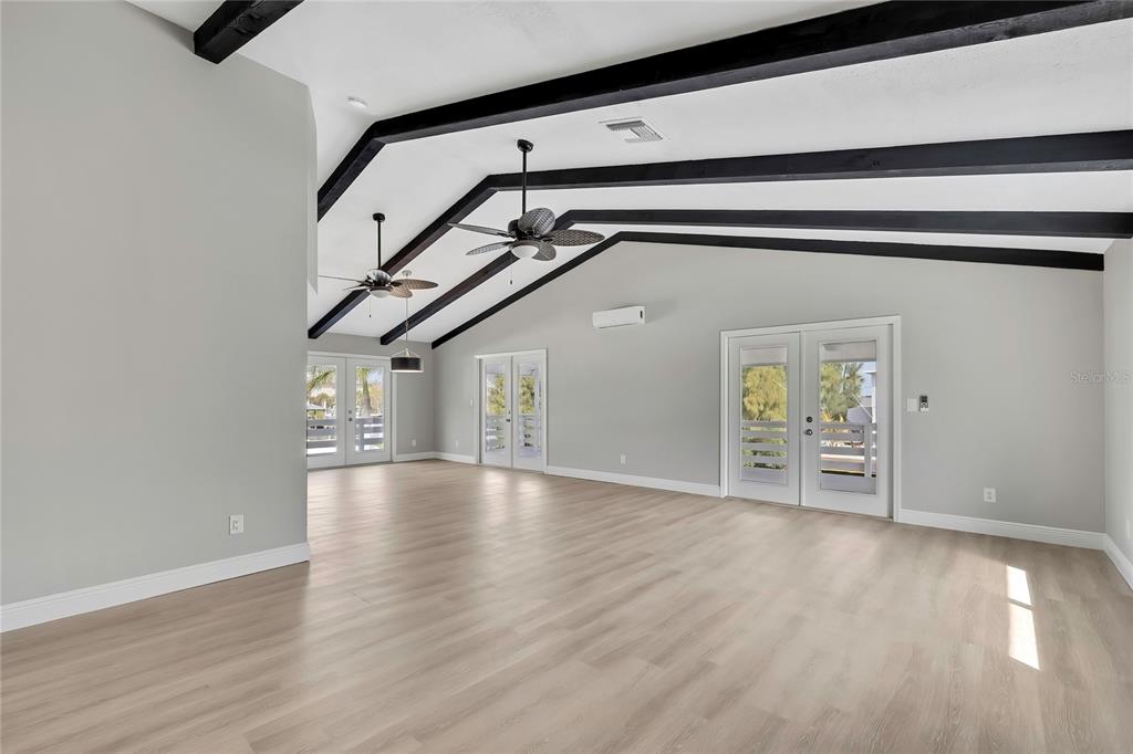 A spacious room with light wood flooring, vaulted ceilings with black beams, and three glass doors — 6703 SEAVIEW BOULEVARD, HUDSON, FL
