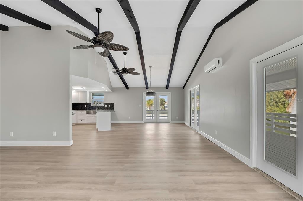 A spacious living area with vaulted ceilings, exposed black beams, light wood floors, and kitchen — 6703 SEAVIEW BOULEVARD, HUDSON, FL