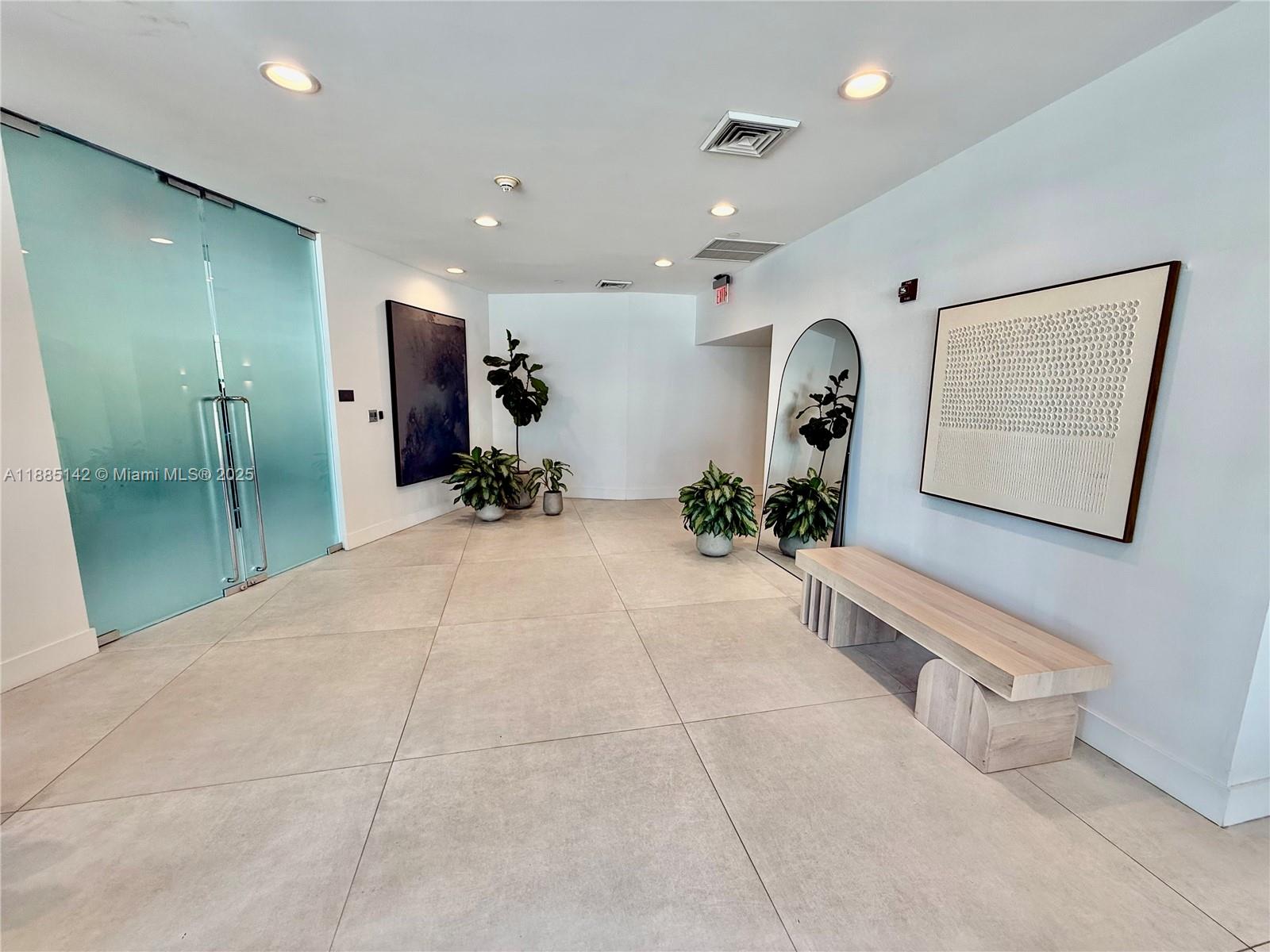 A modern lobby features large light-colored floor tiles, a glass door, plants, and a bench — 1250 S Miami # 1603, Miami FL 33130, MIAMI, FL