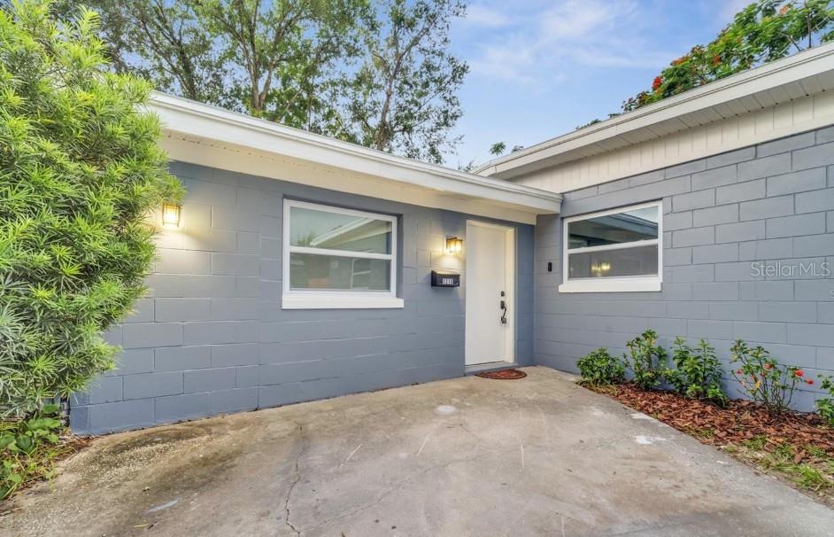 The exterior of a gray concrete block house features a white front door and windows — 1318 TERRE CIA AVENUE, ORLANDO, FL