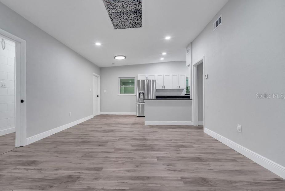 A bright, open-concept room features light gray walls, wood-look flooring, and a kitchen with white cabinets — 1318 TERRE CIA AVENUE, ORLANDO, FL