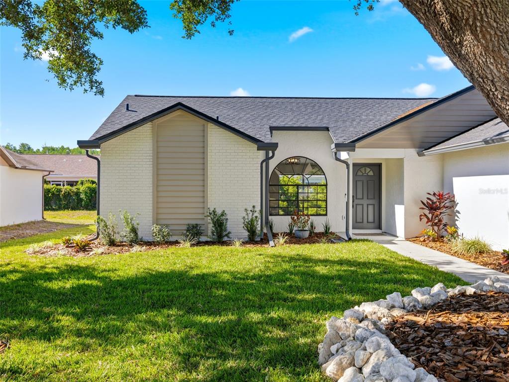 A single-story house with a white brick facade, arched window, and a dark front door — 8452 YEARLING LANE, NEW PORT RICHEY, FL