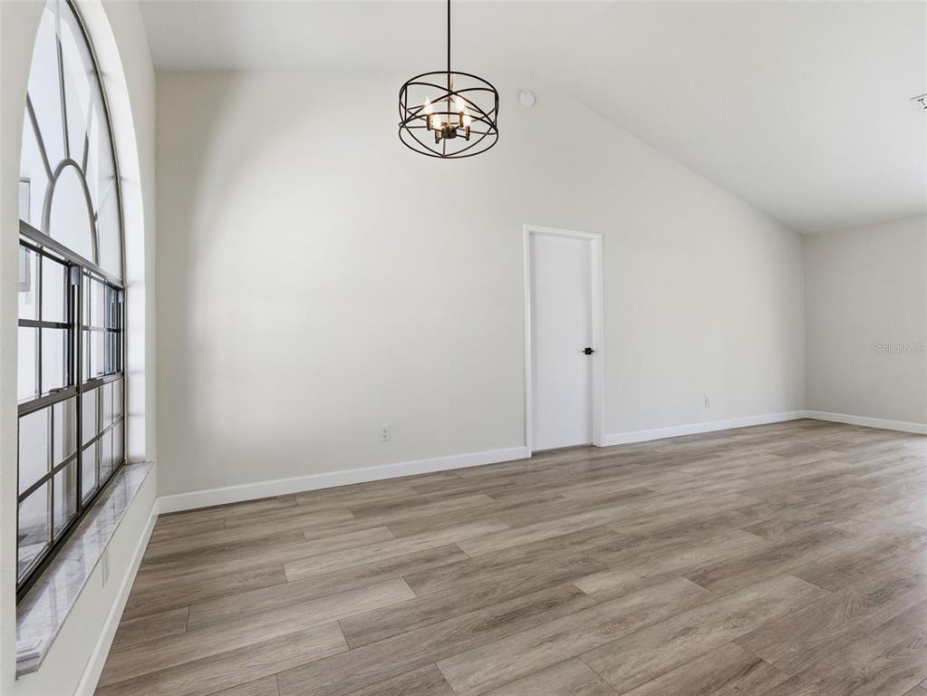 An empty room features light-colored walls, wood-look flooring, a large arched window, and a chandelier — 8452 YEARLING LANE, NEW PORT RICHEY, FL