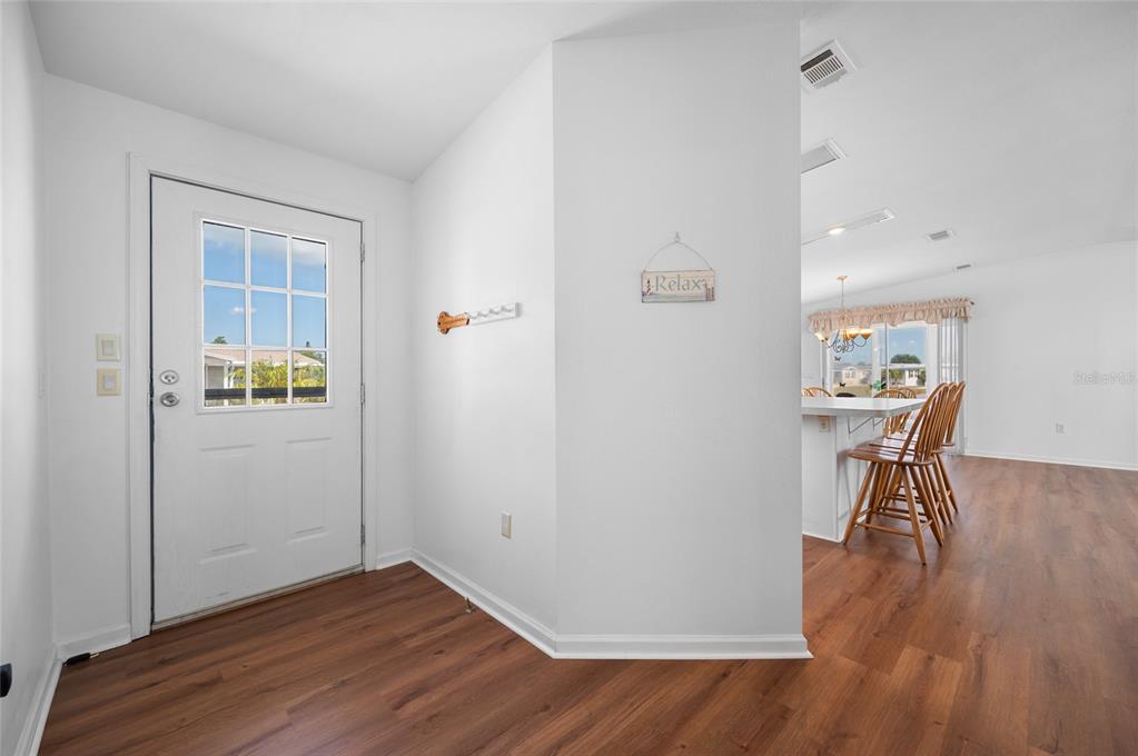An entryway with wood-look flooring leads into an open-concept kitchen with a breakfast bar — 9177 PINEHAVEN WAY, ENGLEWOOD, FL